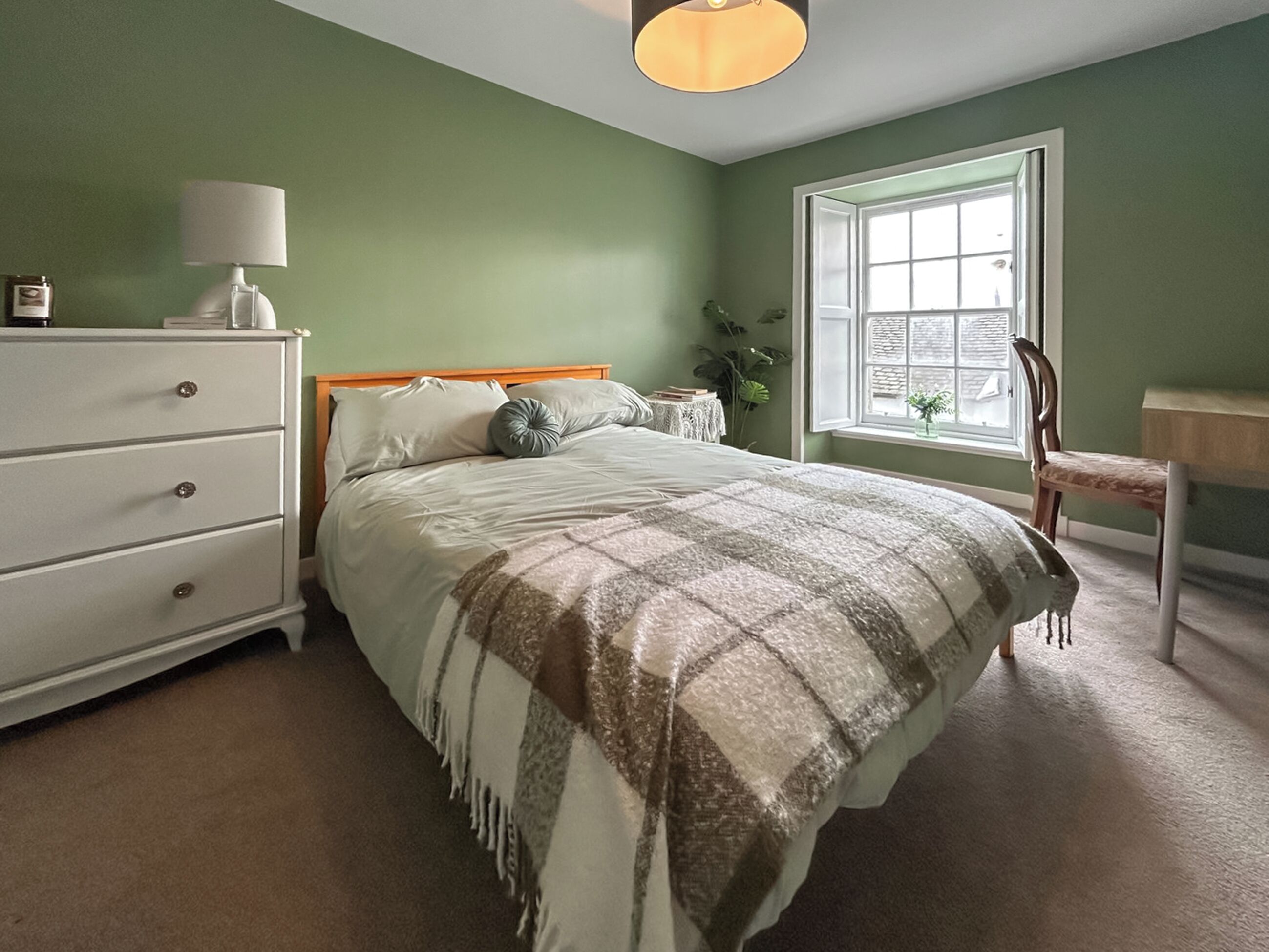 A bedroom with a bed, a dresser, a chair, a window, and a lamp.