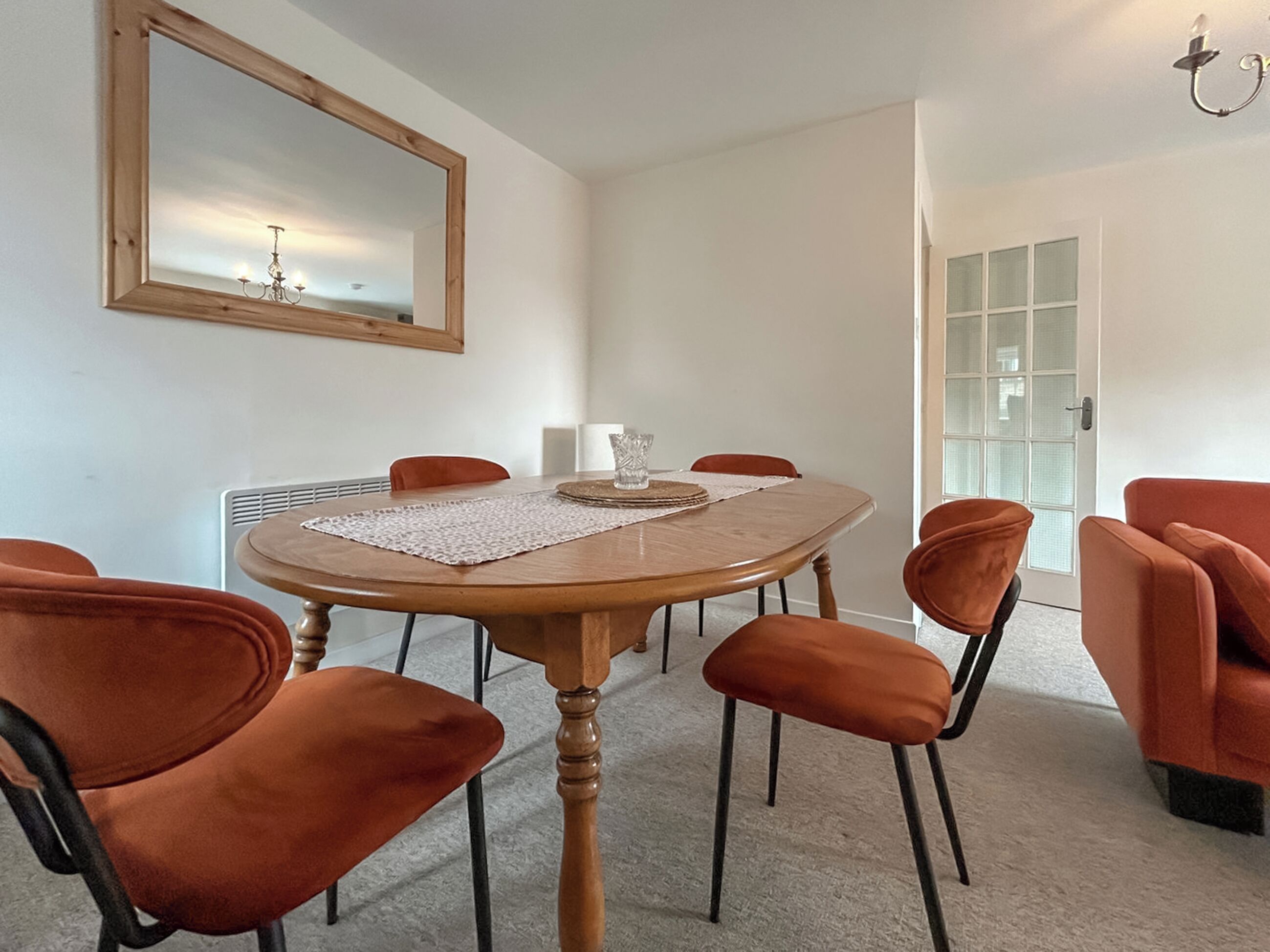 Un coin repas comprenant une table ronde, six chaises, un lustre et un grand miroir au mur.