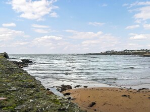 Une plage côtière avec un rivage rocheux, des vagues et une vue lointaine sur des maisons.