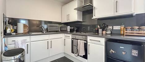 A modern kitchen with white cabinets, a stainless steel range hood, a microwave, and a dishwasher.