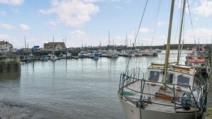 En småbåtshamn med flera båtar förtöjda, en träbrygga och byggnader i bakgrunden.