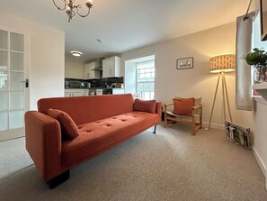 A living room with a sofa, a chair, a floor lamp, and a kitchen in the background. - Elegant, homey Anstruther apartment with sea views and fresh coastal air. (Anstruther)