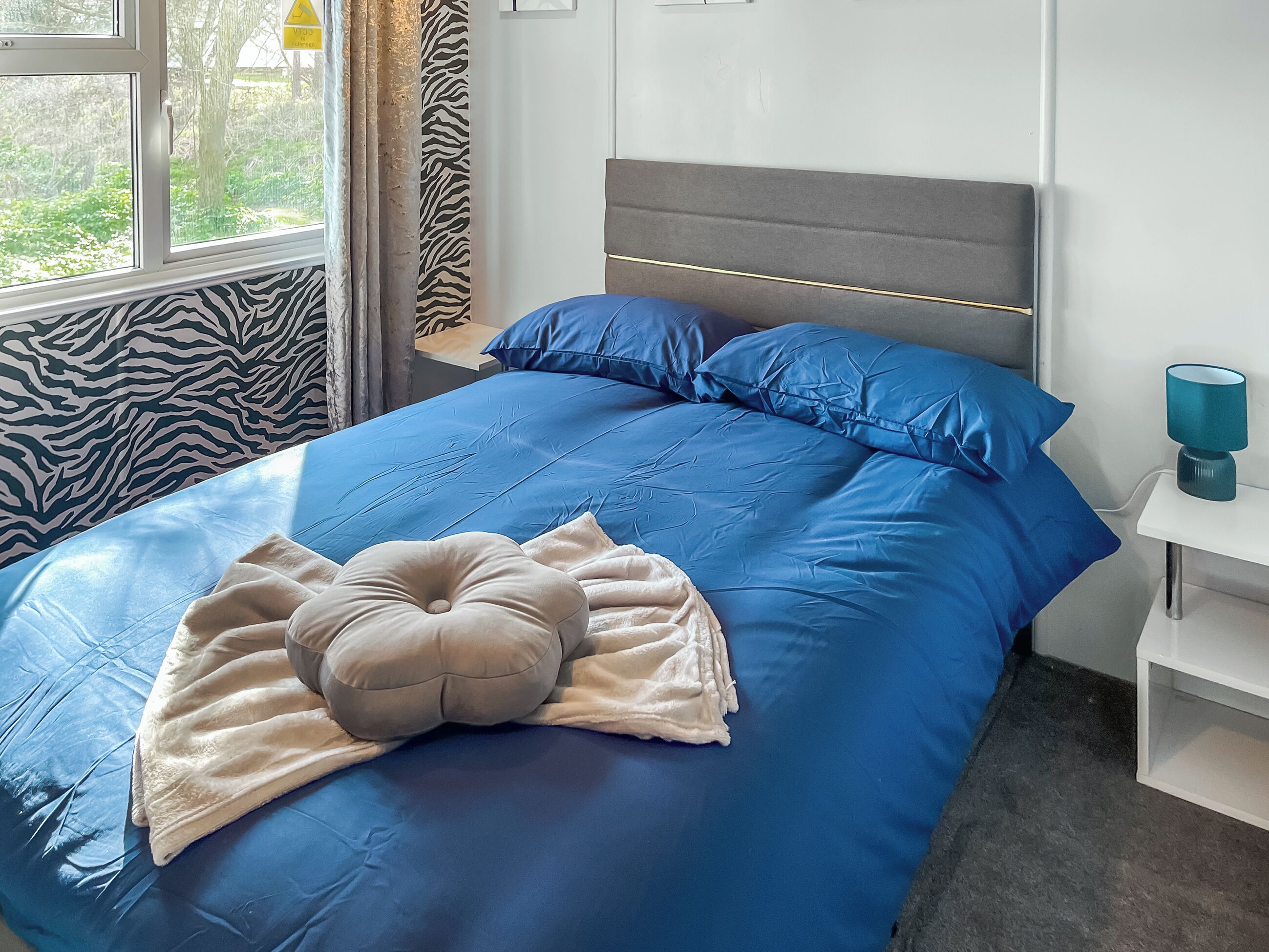 A bedroom with a bed, pillows, a bedside table, and a window.