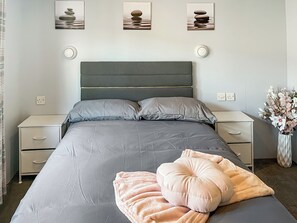 A neatly arranged bedroom with a bed, bedside tables, a nightstand, and wall-mounted light fixtures. - 3 bedroom accommodation in Corton (Corton)