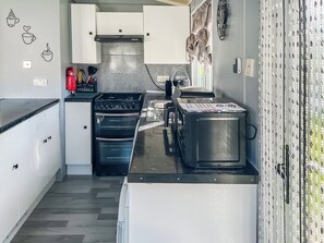 Een kleine keuken met witte kasten, een inbouwoven, een koffiezetapparaat en een roestvrijstalen afzuigkap.