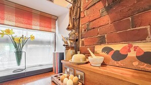 A kitchen with a wooden countertop, a window with a view, a vase of daffodils, and a rooster painting. - 1 bedroom accommodation in Bosbury (Bosbury)