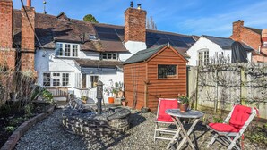 A garden with a stone fountain, two red chairs, and a wooden shed. - 1 bedroom accommodation in Bosbury (Bosbury)