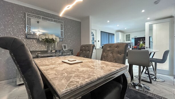 Un coin repas avec une table en marbre, des chaises à revêtement noir, un lustre moderne et une cuisine en arrière-plan.