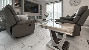 Un salon moderne avec deux fauteuils inclinables en cuir, une table basse en marbre, un téléviseur à écran plat et une horloge murale.