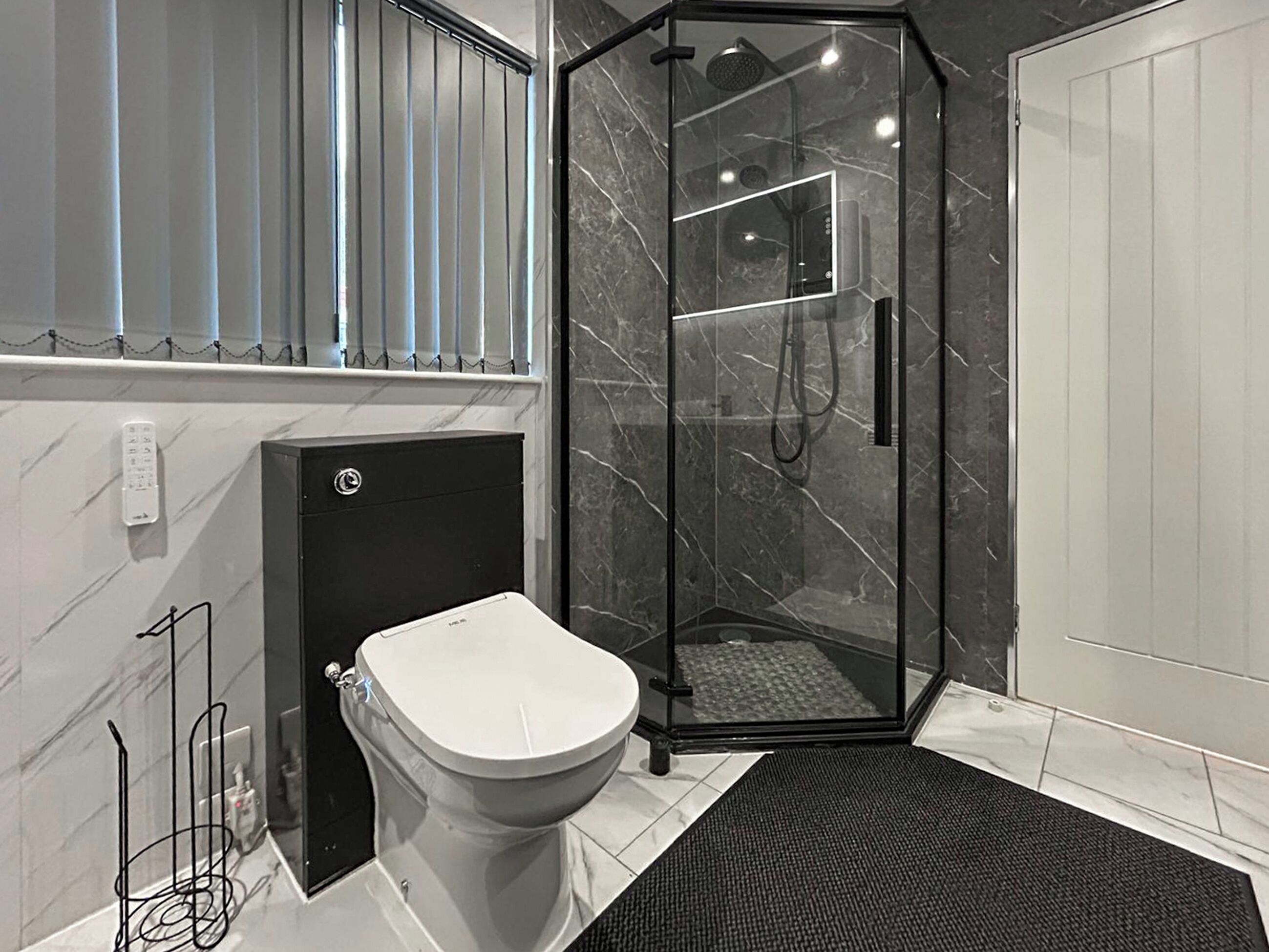 A modern bathroom with a glass-enclosed shower, a toilet, and a marble-tiled floor.
