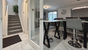 Un intérieur moderne avec un escalier, un coin repas doté de tabourets de bar et une grande horloge au mur.