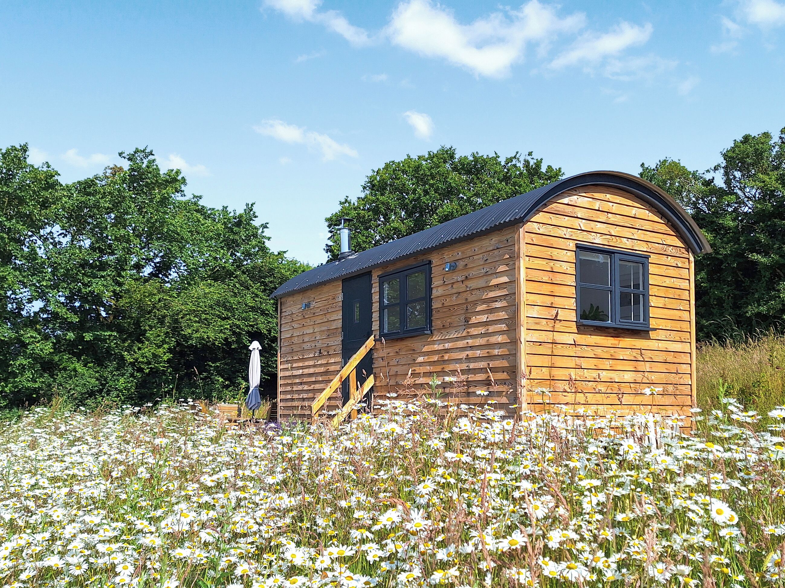 A wooden cabin with a curved roof, two windows, and a small porch with a chair.
