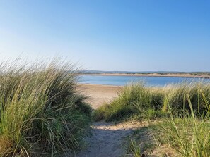 Un sendero bordeando la playa que lleva a un mar tranquilo, con dunas al fondo.