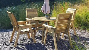 Un conjunto de mesa y sillas de madera sobre grava, con una sombrilla de metal.