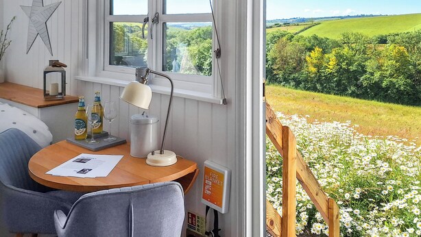 Una habitación con un escritorio de madera, una lámpara, un adorno con forma de estrella y una ventana que da a un campo de flores.