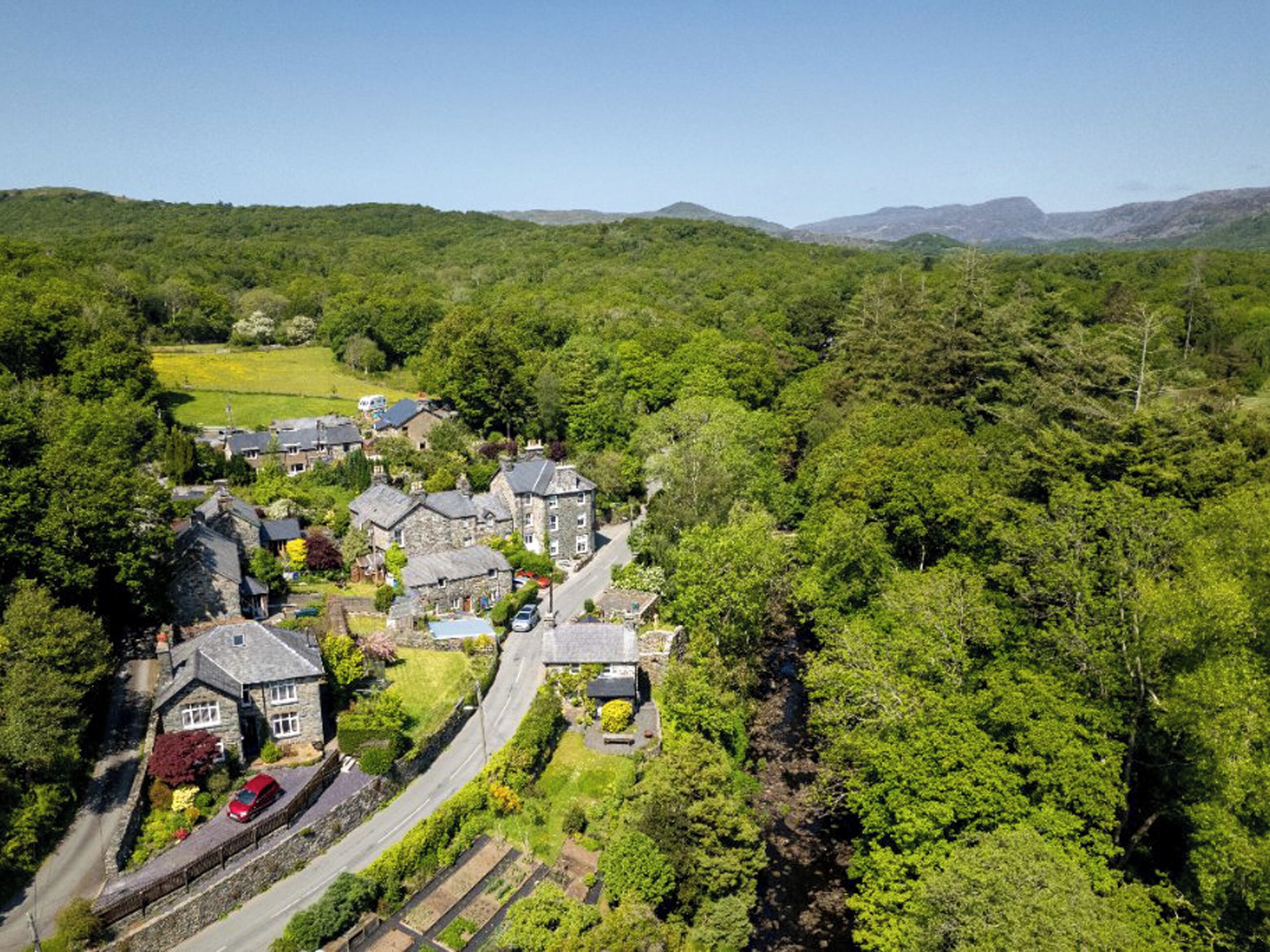 A rural village with stone houses, a winding road, and lush greenery.