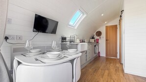 Une cuisine moderne avec un coin repas, des meubles blancs, un téléviseur à écran plat et une lucarne.