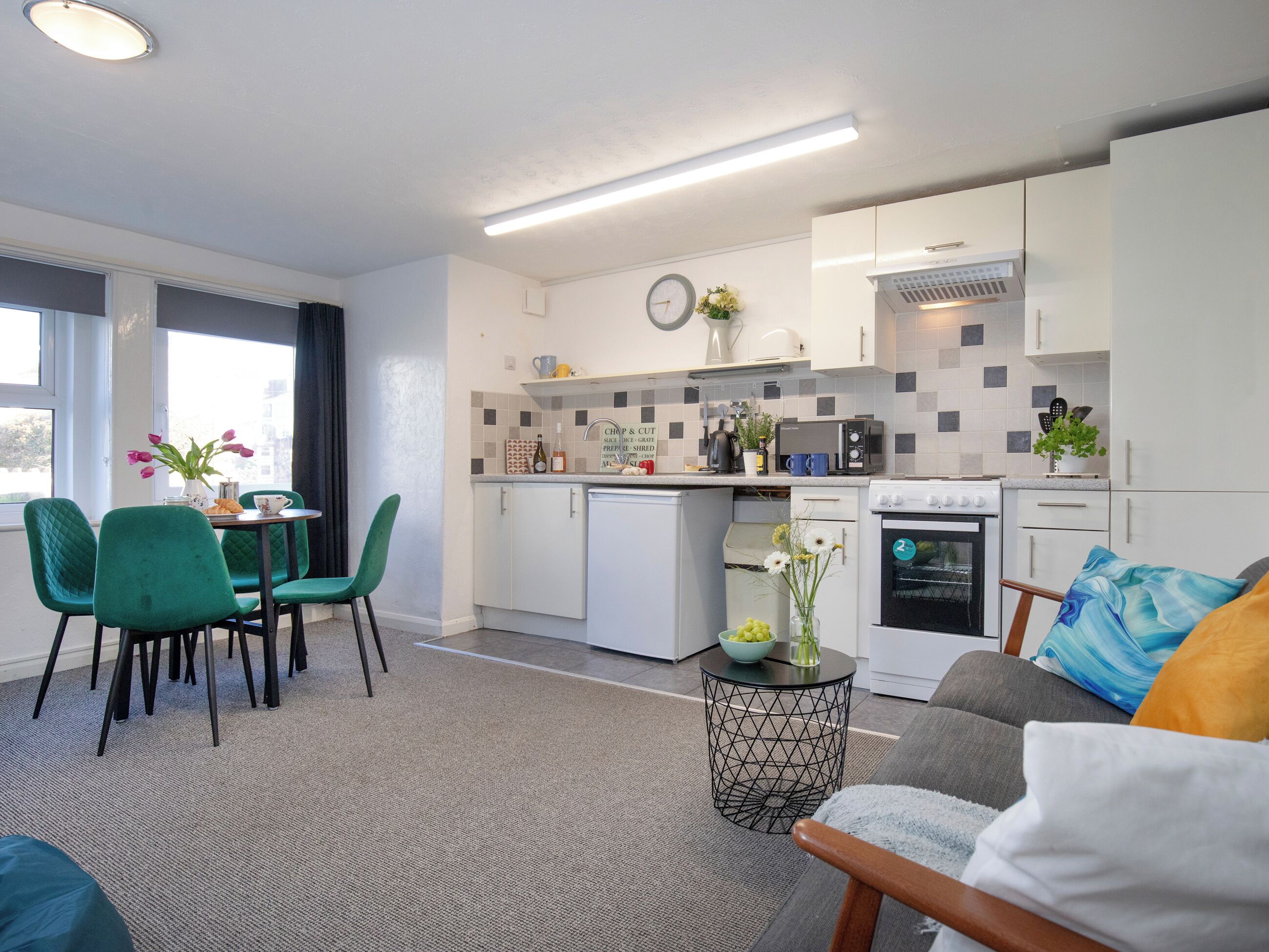 A compact living space with a kitchenette, a dining area with chairs, a sofa, and a small side table.