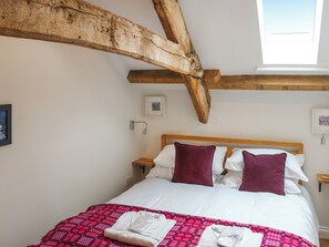 Un dormitorio con techo de madera, una cama con almohadas blancas y burdeos, una colcha de edredón estampada en rosa y una ventana con vistas.