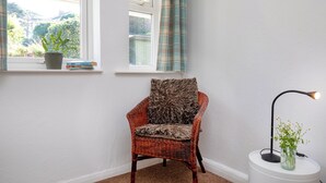 A corner room with a wicker chair, a small table with a lamp, a window with curtains, and a potted plant. - Bay Tree View - UK51428 (Paignton)