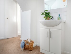 A bathroom with a white sink, a plant, a bottle of Palmolive soap, and a woven basket with a blue towel. - Bay Tree View - UK51428 (Paignton)