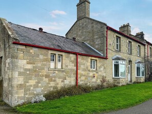 A stone building with a red pipe running along the side, a chimney, and a grassy lawn. - 2 bedroom accommodation in Morpeth (Morpeth)
