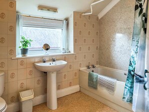 A bathroom with a sink, toilet, bathtub, and window with a plant. - 2 bedroom accommodation in Morpeth (Morpeth)