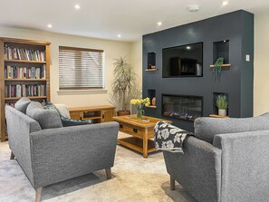 A living room with a fireplace, a bookshelf, and a TV mounted on the wall. - Pet friendly one-bedroom annex, perfect for couples or two friends. (Armathwaite)