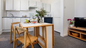 A modern kitchen with white cabinets, a dining table with chairs, a microwave, and a TV on a stand. - A comfortable first-floor apartment for two with lovely sea views. (Paignton)