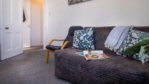 A room with a dark brown quilted sofa, a wooden chair, a door, and a painting of a coastal scene.