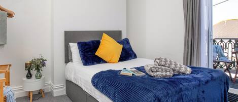 A neatly arranged bedroom with a bed, bedside tables, a small plant, and a view of the outside.