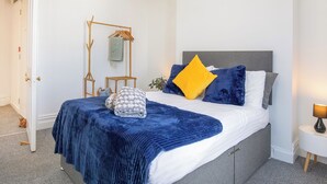 A bedroom with a bed, a bedside table, a hanging light, and a door.