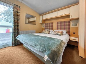 A bedroom with a bed, a window with curtains, a radiator, a mirror, and a bedside table. - 2 bedroom accommodation in Angus (Edinburgh and the Lothians)