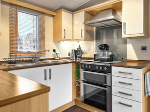A compact kitchen with a sink, stove, oven, and a window with blinds. - 2 bedroom accommodation in Angus (Edinburgh and the Lothians)