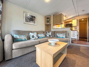 A living room with a sofa, a coffee table, a painting, and a kitchen area. - 2 bedroom accommodation in Angus (Edinburgh and the Lothians)