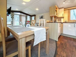 A compact kitchen with wooden cabinets, a dining table with chairs, and a window with blinds. - 2 bedroom accommodation in Angus (Edinburgh and the Lothians)