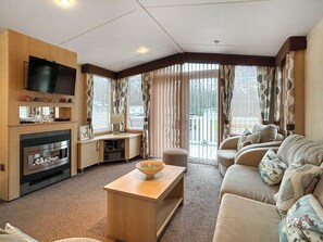 A living room with a fireplace, television, sofa, and a view through large windows. - 2 bedroom accommodation in Angus (Edinburgh and the Lothians)