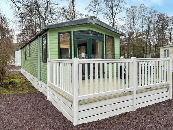A small, single-story structure with a white deck and green siding, surrounded by trees. - 2 bedroom accommodation in Angus (Edinburgh and the Lothians)