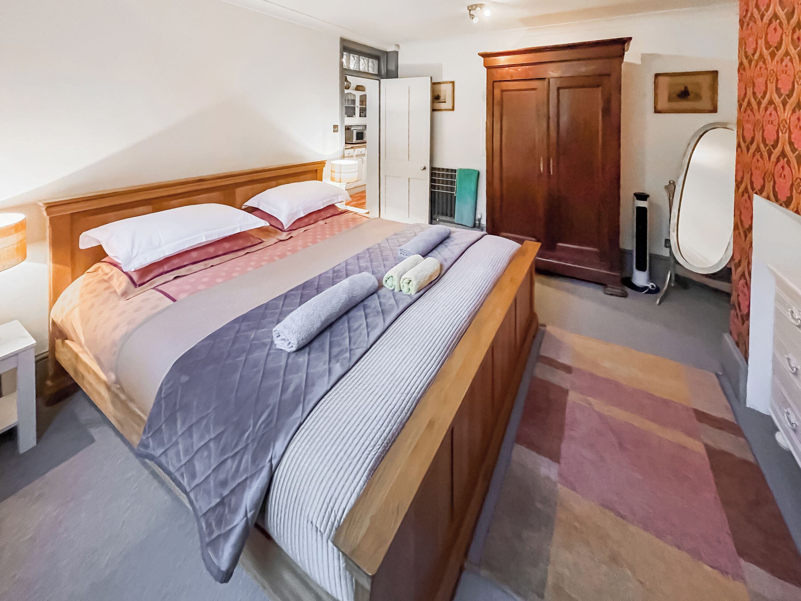 A bedroom with a bed, a wardrobe, a mirror, and a nightstand.