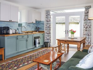 Eine gemütliche Küche mit einem Holztisch, einem grünen Sofa, einem gemusterten Teppich und einem Fenster mit Vorhängen.