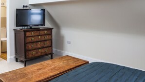 Een slaapkamer met een bed, een houten dressoir met lades, een televisie erop en een klein houten bankje.