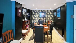 A dining area with a wooden table and chairs, a bookshelf, a clock, and a television on the wall. - 3 bedroom accommodation in Ramsgate (Ramsgate)