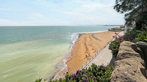 A beach with a clear view of the ocean, a paved walkway, and a rocky cliff with vegetation. - 3 bedroom accommodation in Ramsgate (Ramsgate)
