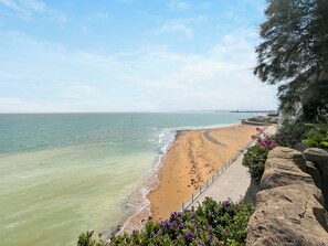 A beach with a clear view of the ocean, a paved walkway, and a rocky cliff with vegetation. - 3 bedroom accommodation in Ramsgate (Ramsgate)
