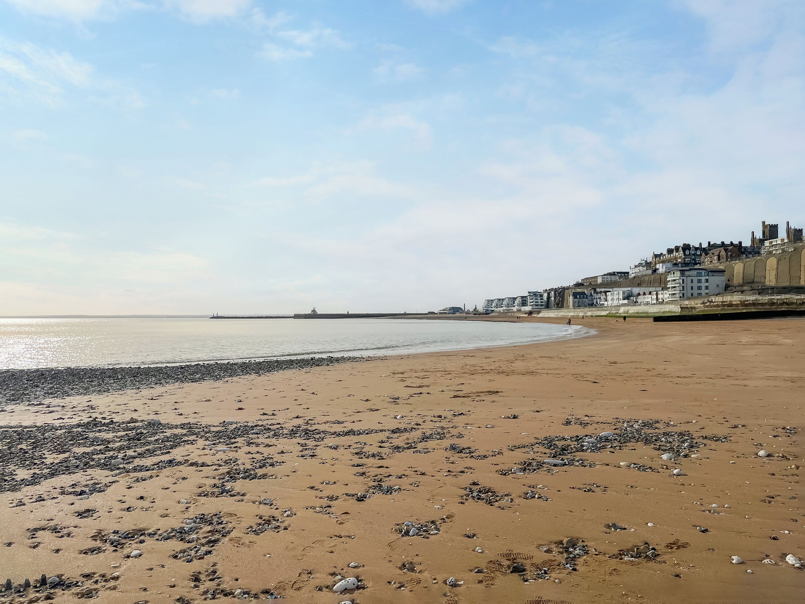 A beach with pebbles and a distant view of buildings.