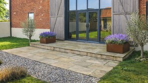 A brick building with a large sliding glass door, a gravel pathway, and two flower planters. - 5 bedroom accommodation in Heydon (Heydon)