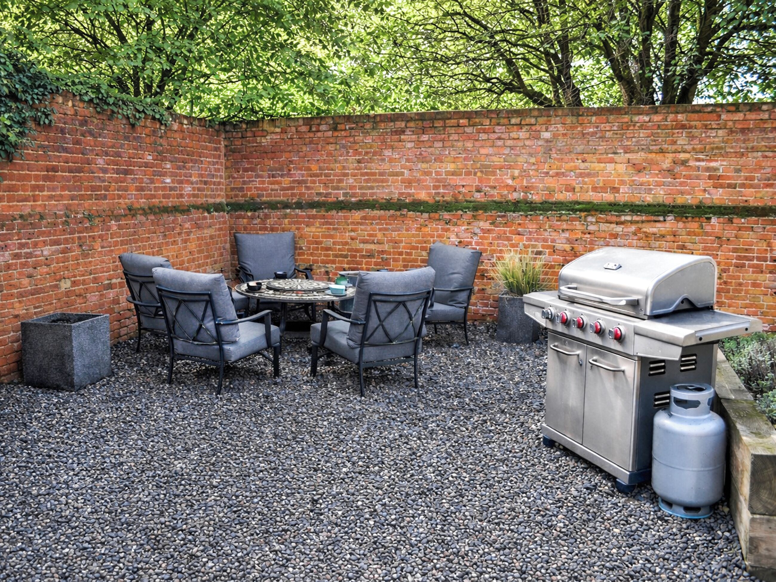 A patio with a brick wall, a grill, and four chairs.