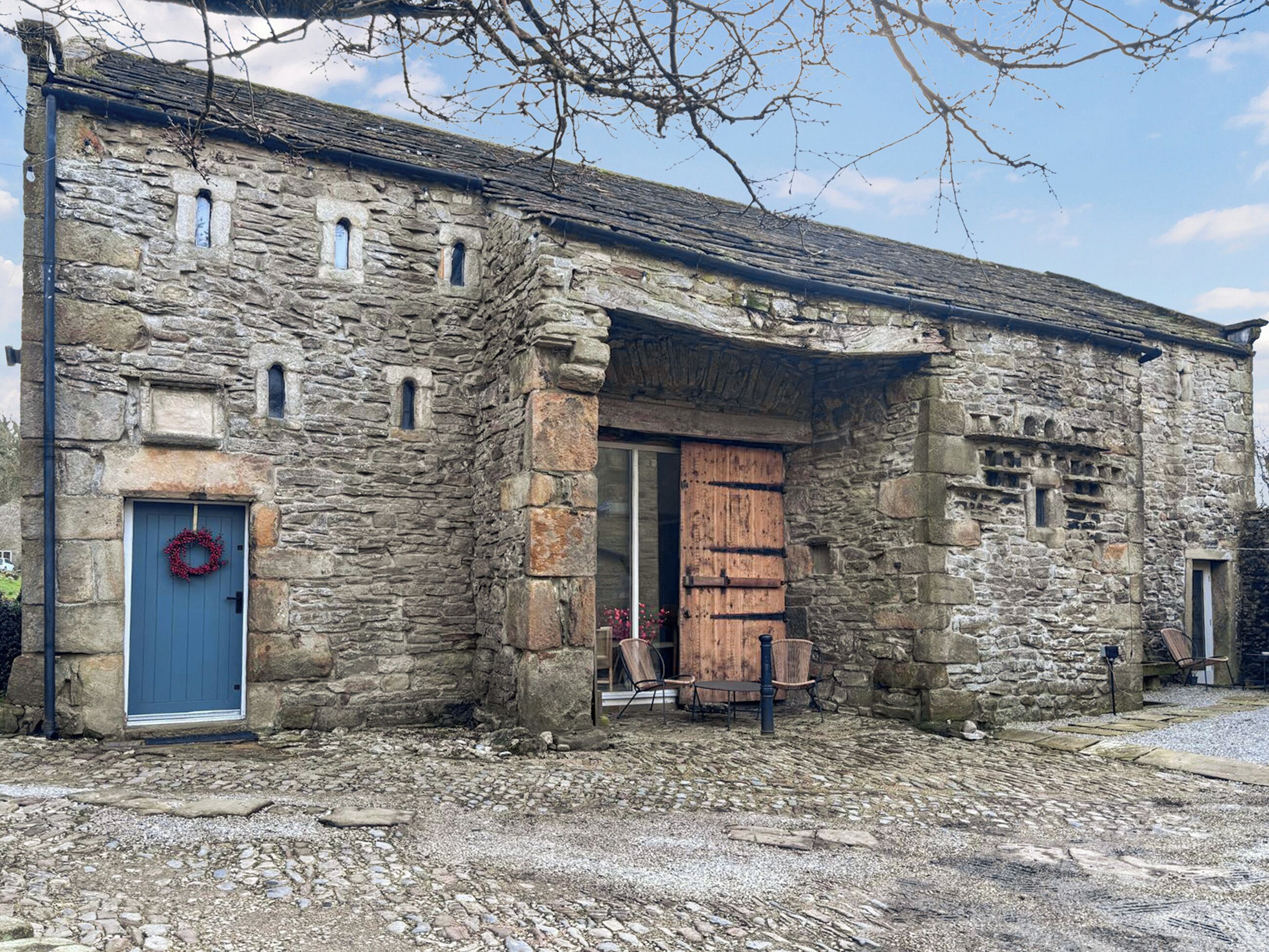 Un edificio de piedra con una puerta azul y una puerta de madera, un patio de grava y un adorno en la puerta.