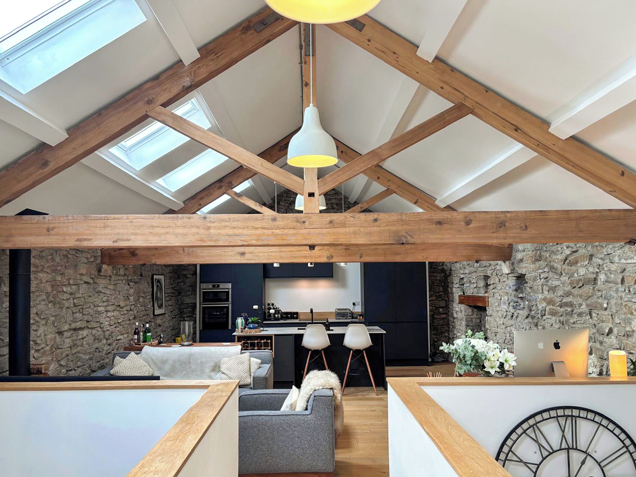 A spacious loft with exposed wooden beams, a stone wall, a kitchen area, and a seating area with a sofa and chairs.