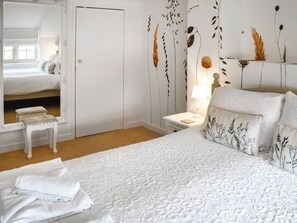 A bedroom with a bed, a nightstand, a mirror, and a wall with floral wallpaper. - Welcoming larger family gatherings. (Winterton-on-Sea)